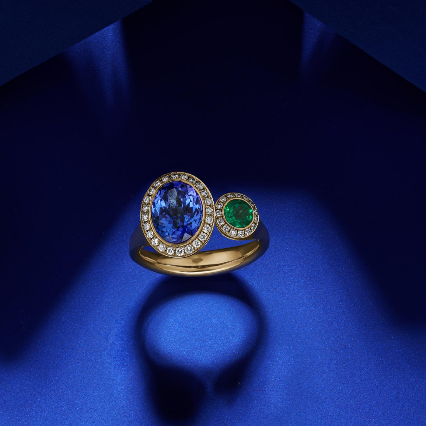 Toi et moi ring featuring an oval-shaped tanzanite and a round emerald surrounded by smaller diamonds sophisticated spark designed by carati jewelry in montreal canada in 18 k 14 k in blue backround 2