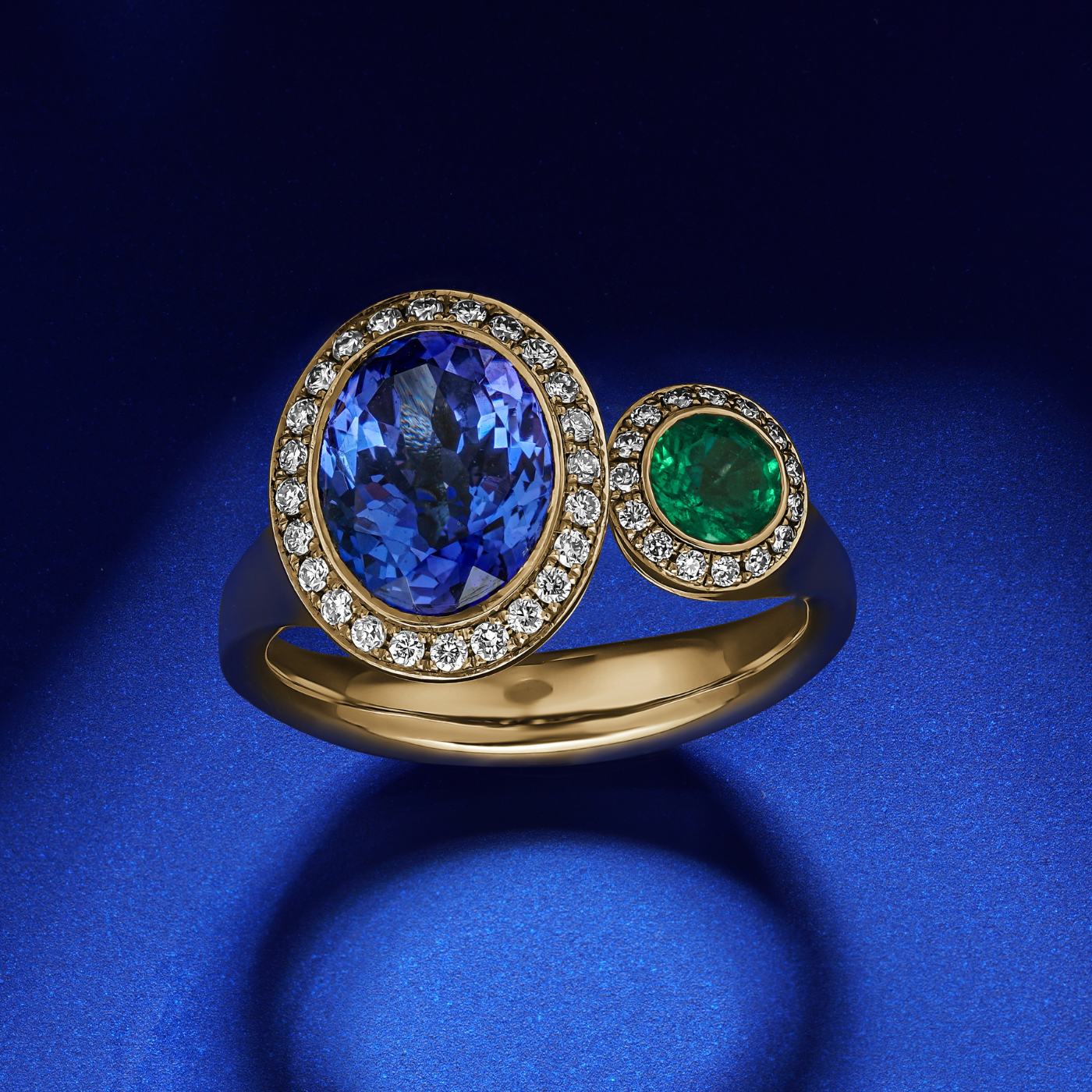 Toi et moi ring featuring an oval-shaped tanzanite and a round emerald surrounded by smaller diamonds sophisticated spark designed by carati jewelry in montreal canada in 18 k 14 k in blue backround