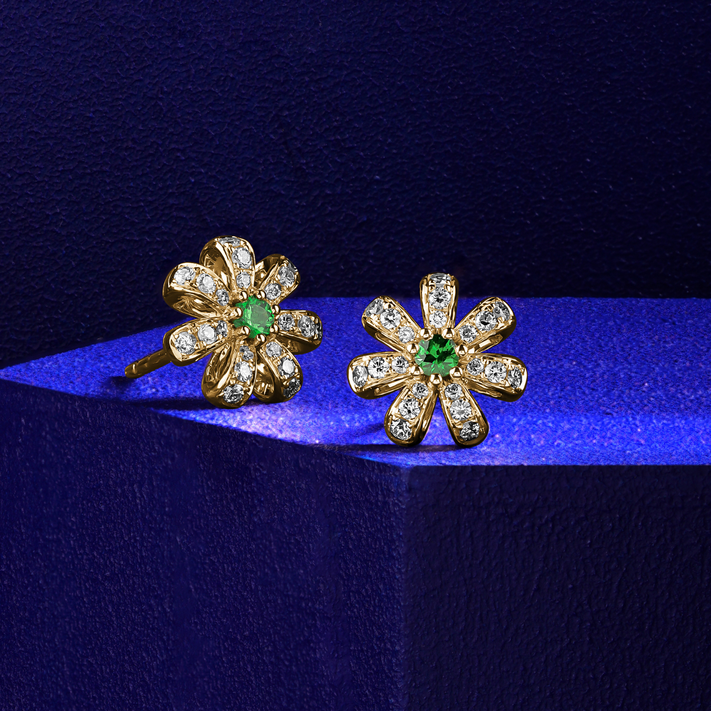 A pair of Fiora earrings with naturaln tsavorites centers and encrusted with diamonds set in pave designed by carati jewelry montreal canada 18k 14 k with blue backround