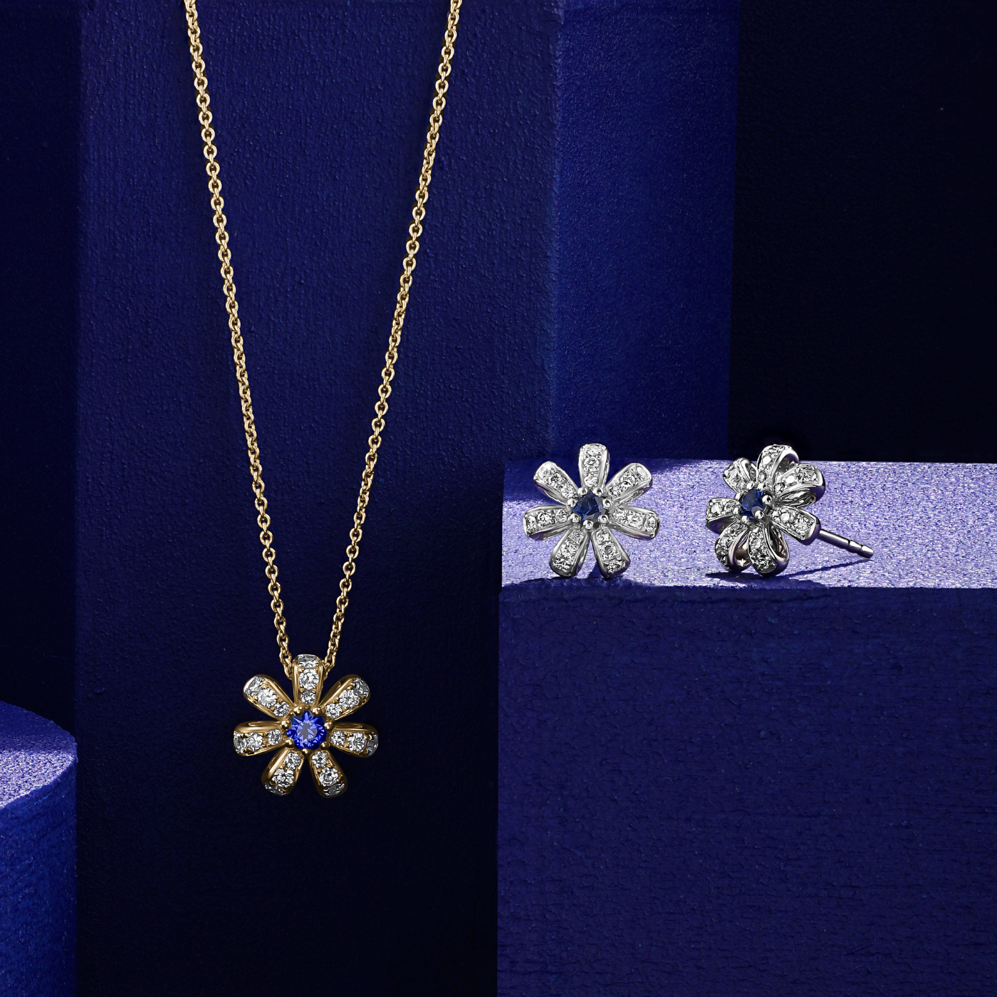 A pair of Fiora earrings with natural royal blue sapphires centers and encrusted with diamonds set in pave designed by carati jewelry montreal canada 18k 14 k in blue backround and pendant