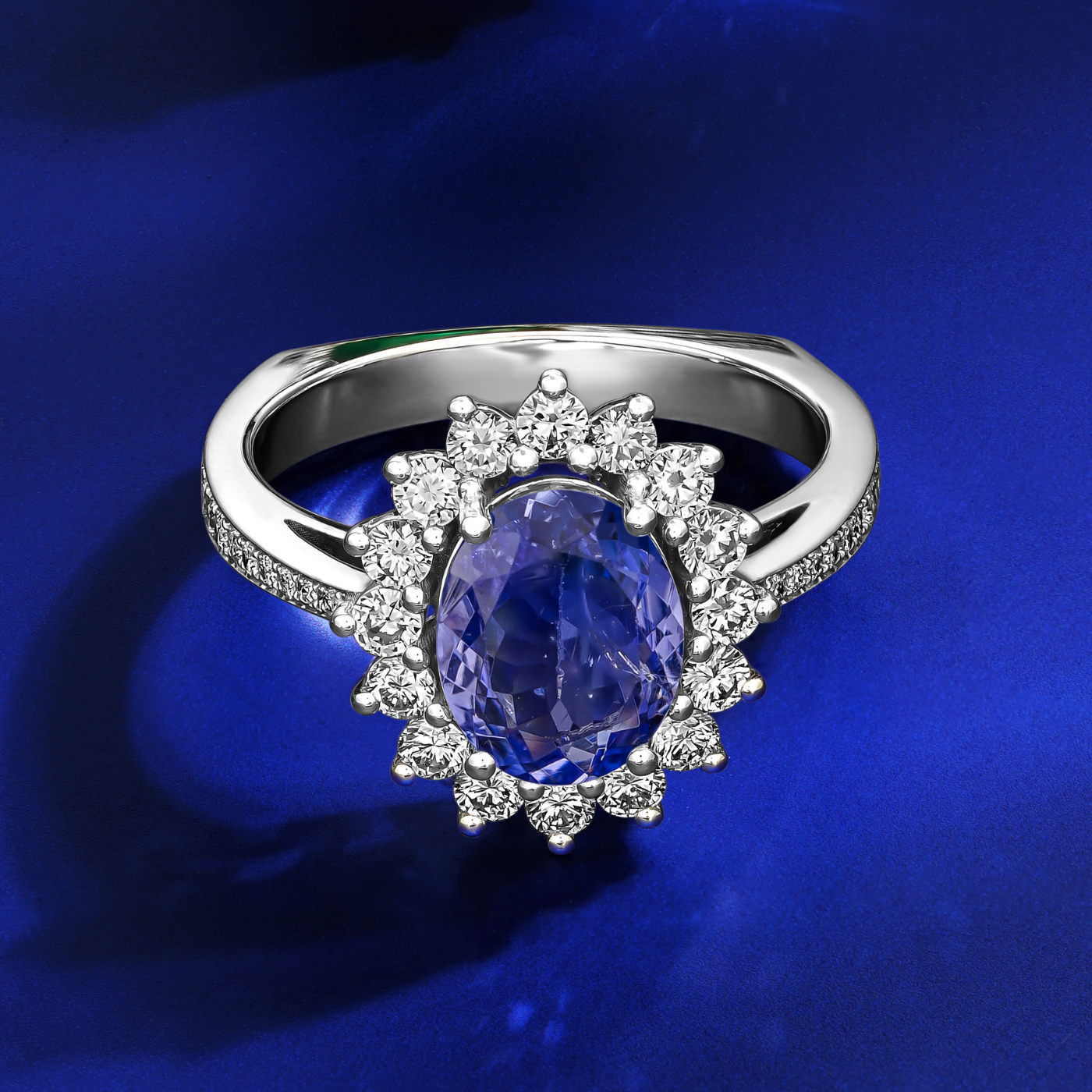 in blue backround An elegant engagement ring with a central oval Tanzanite stone, surrounded by a halo of sparkling diamonds, set in a white gold band designed by carati jewelry in montreal canada 14 k 18 k