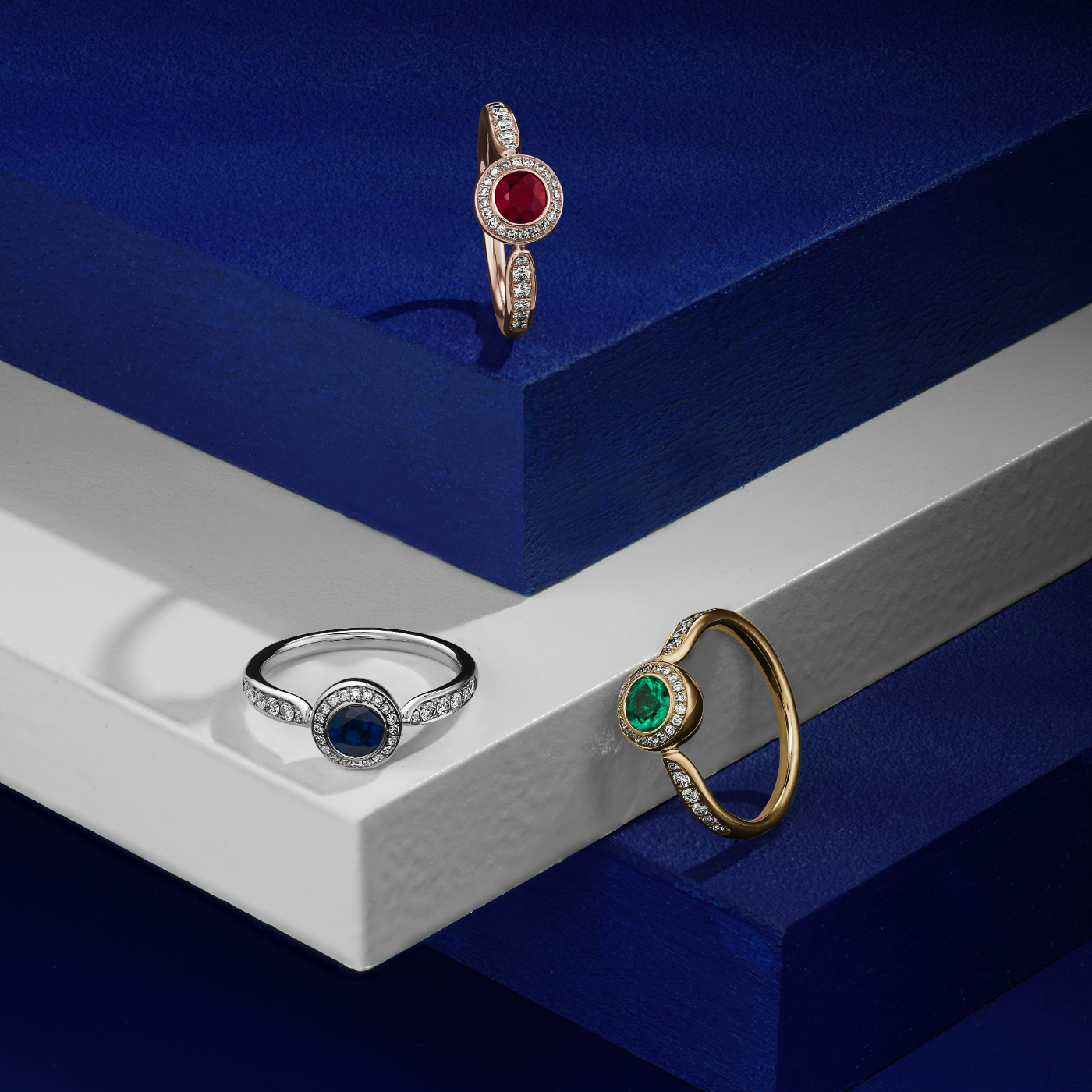 Royal harmony ring with round ruby surrounded by pave diamonds and on the shank designed by carati jewelry in montreal canada 18k 14 k in all 3 rings in blue backround