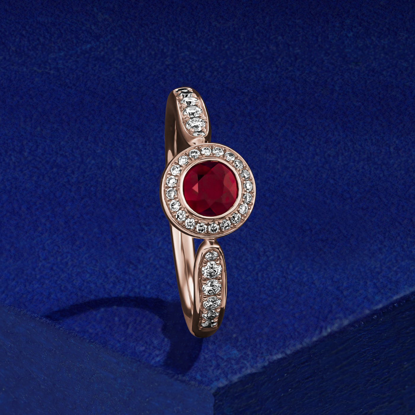 Royal harmony ring with round ruby surrounded by pave diamonds and on the shank designed by carati jewelry in montreal canada 18k 14 k in blue backround