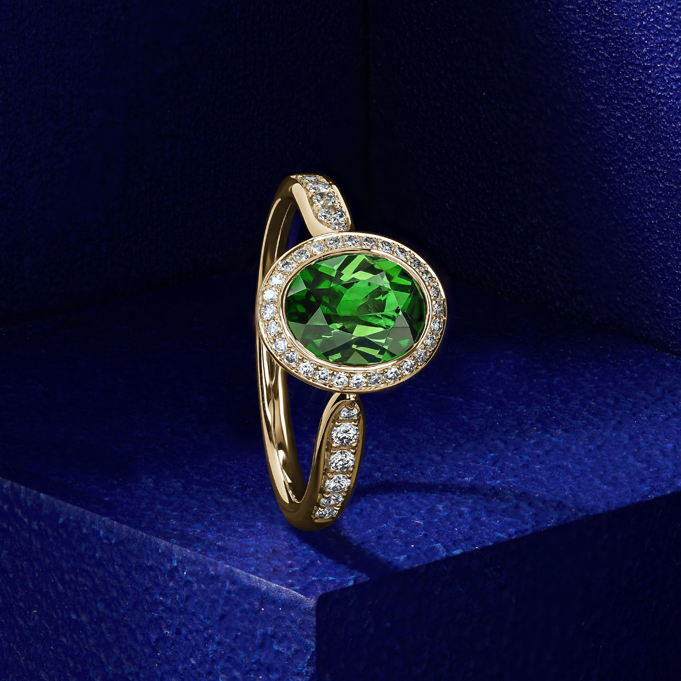 Royal harmony ring with oval green tourmaline surrounded by pave diamonds and on the shank designed by carati jewelry in montreal canada 18k 14 k in blue backround