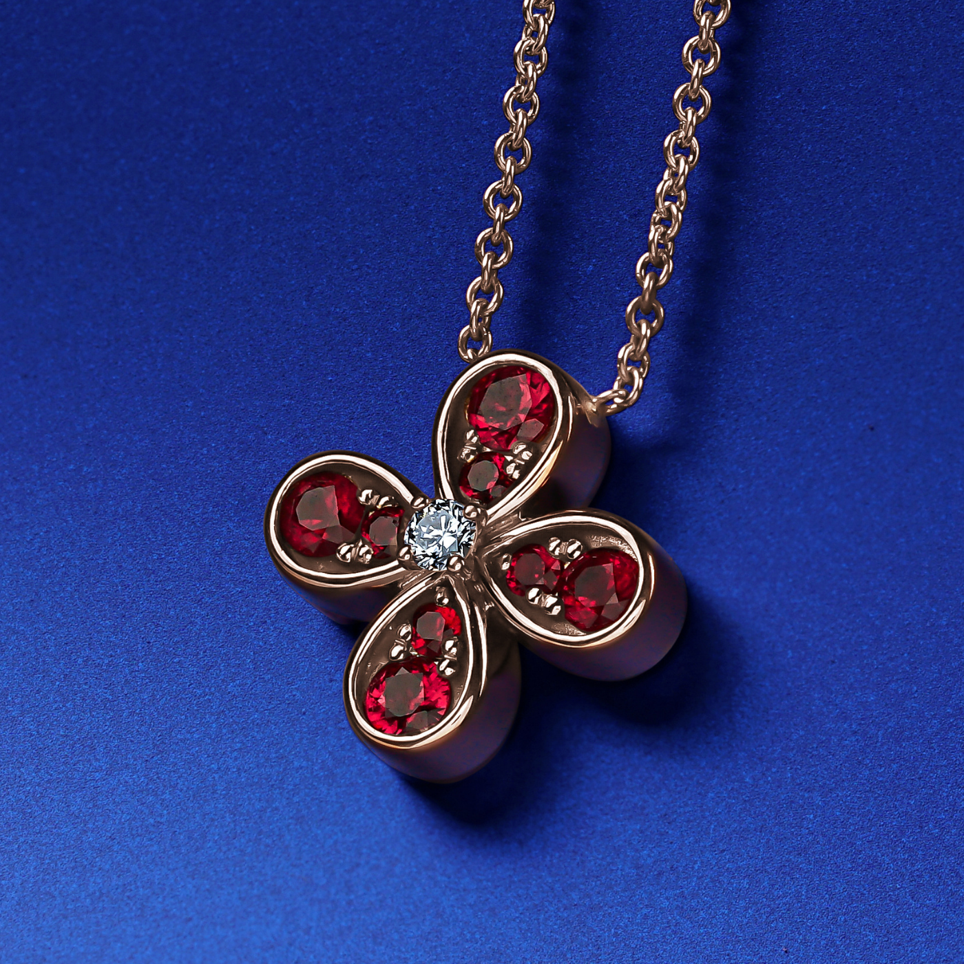 Bloom pendant set in ruby's and a diamond in the middle designed by carati jewelry montreal canada 18k 14 k in blue backround
