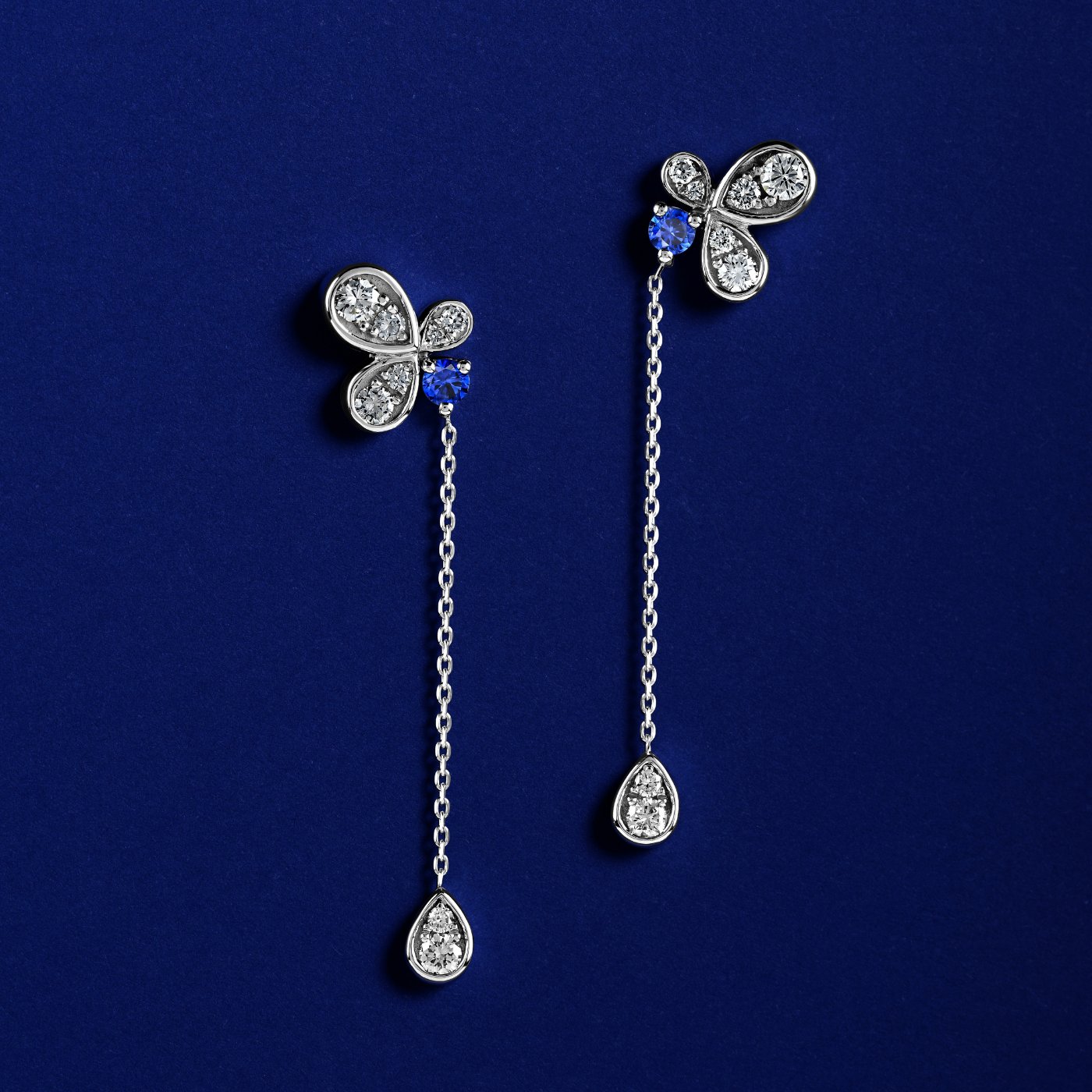 Bloom pair of earrings featuring royal blue sapphires with butterfly designs, connected to diamond-studded chains designed by carati jewelry in montreal canada in 18 k 14 k
