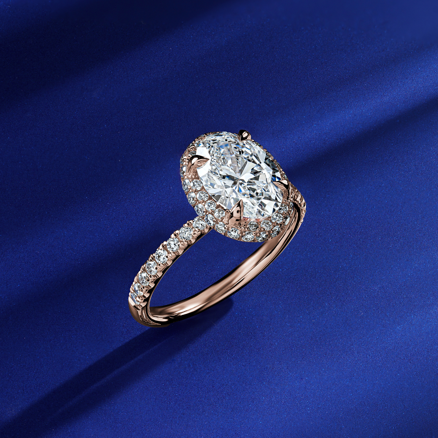 Eterno oval engagement ring set with pave on the top and band in a sophisticated spark designed by carati jewelry in montreal canada in 18 k 14 k in blue backround