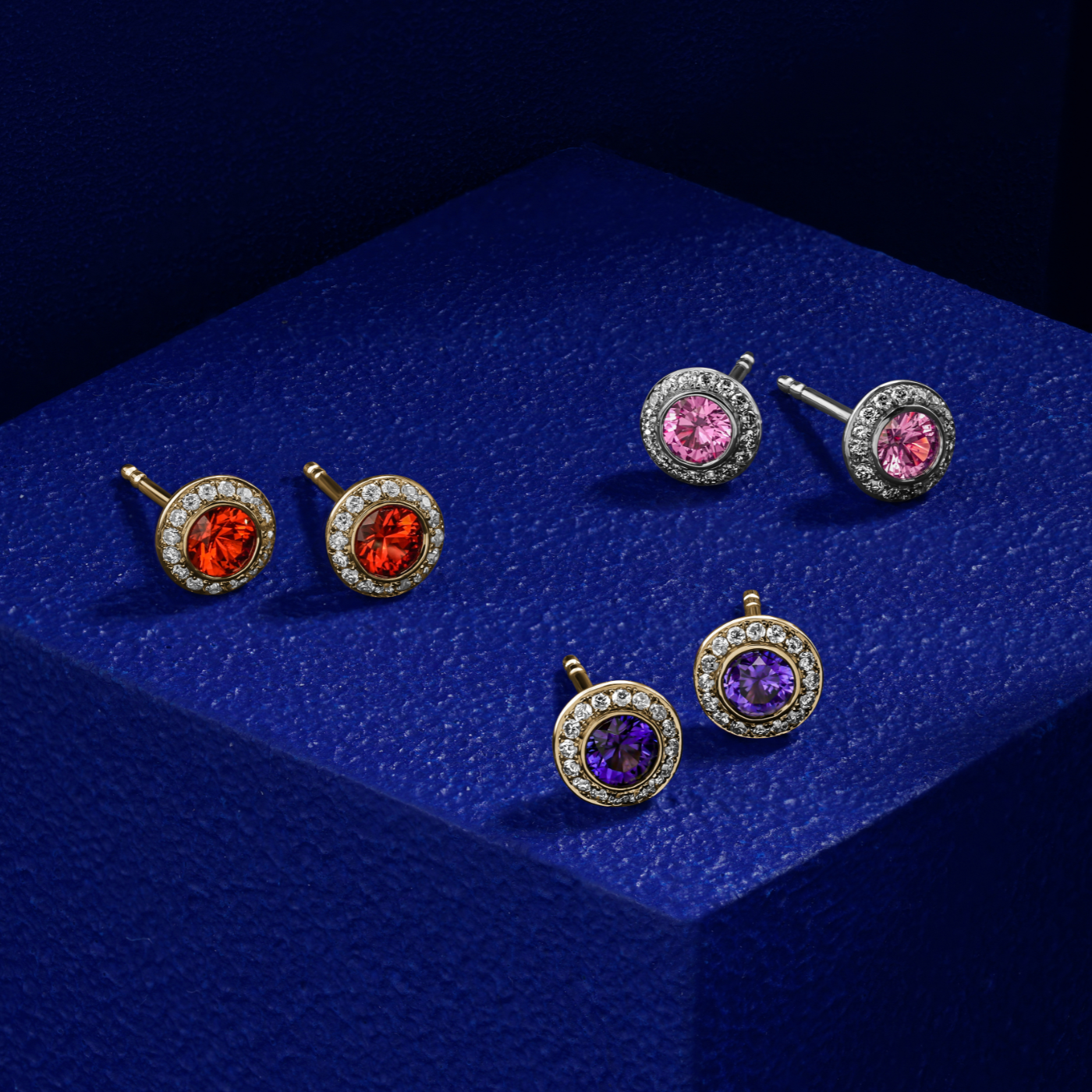 Royal Harmony earring Centered Around a stunning tsavorite set all around pave in diamonds designed by carati jewelry in montreal canada in 14 k 18 k in blue backround with all the other earrings purple pink and orange