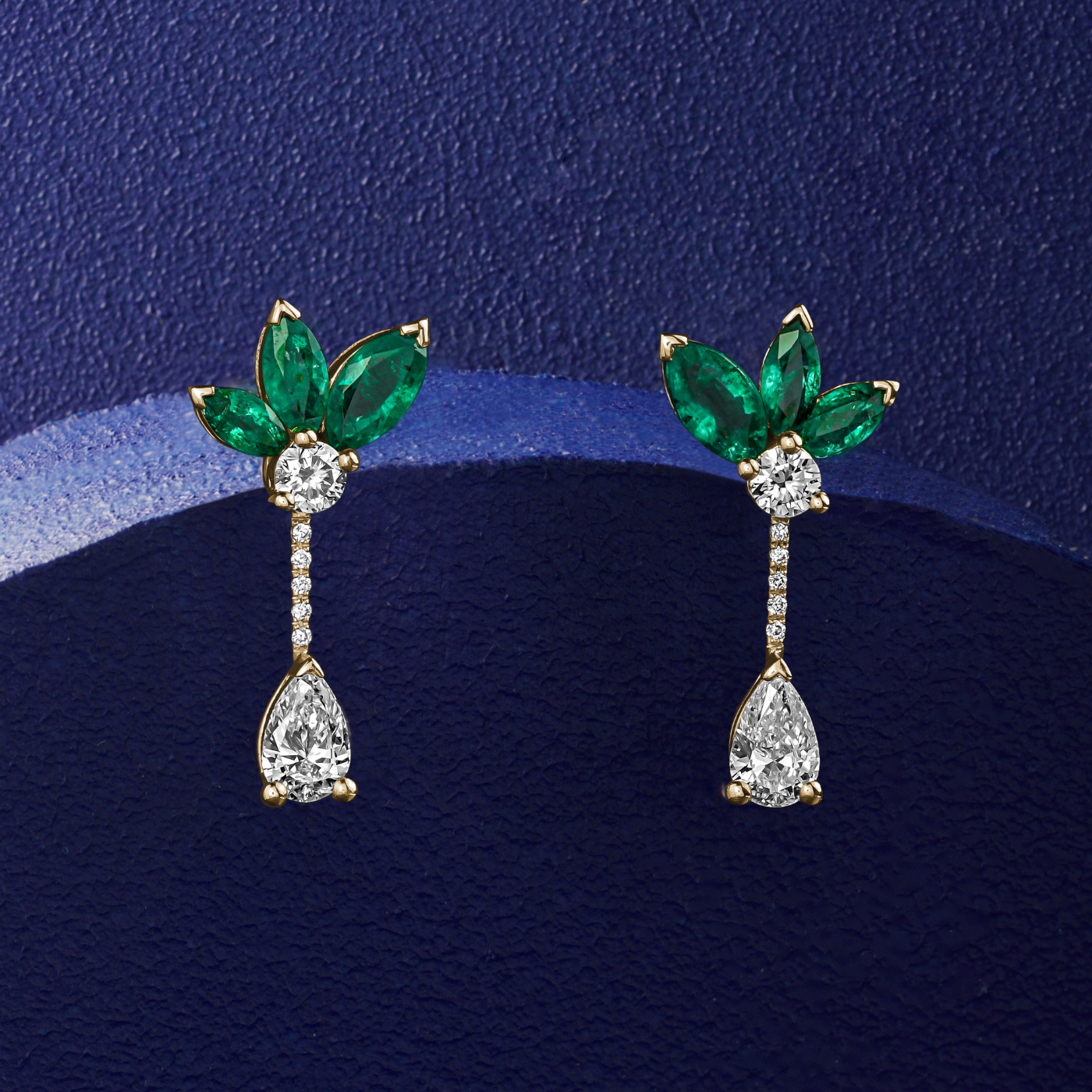 Majesty earrings with marquise  Emeralds and a pear diamond is designed by carati jewelry in Montreal Canada in 14k 18k in blue backround and zoomed