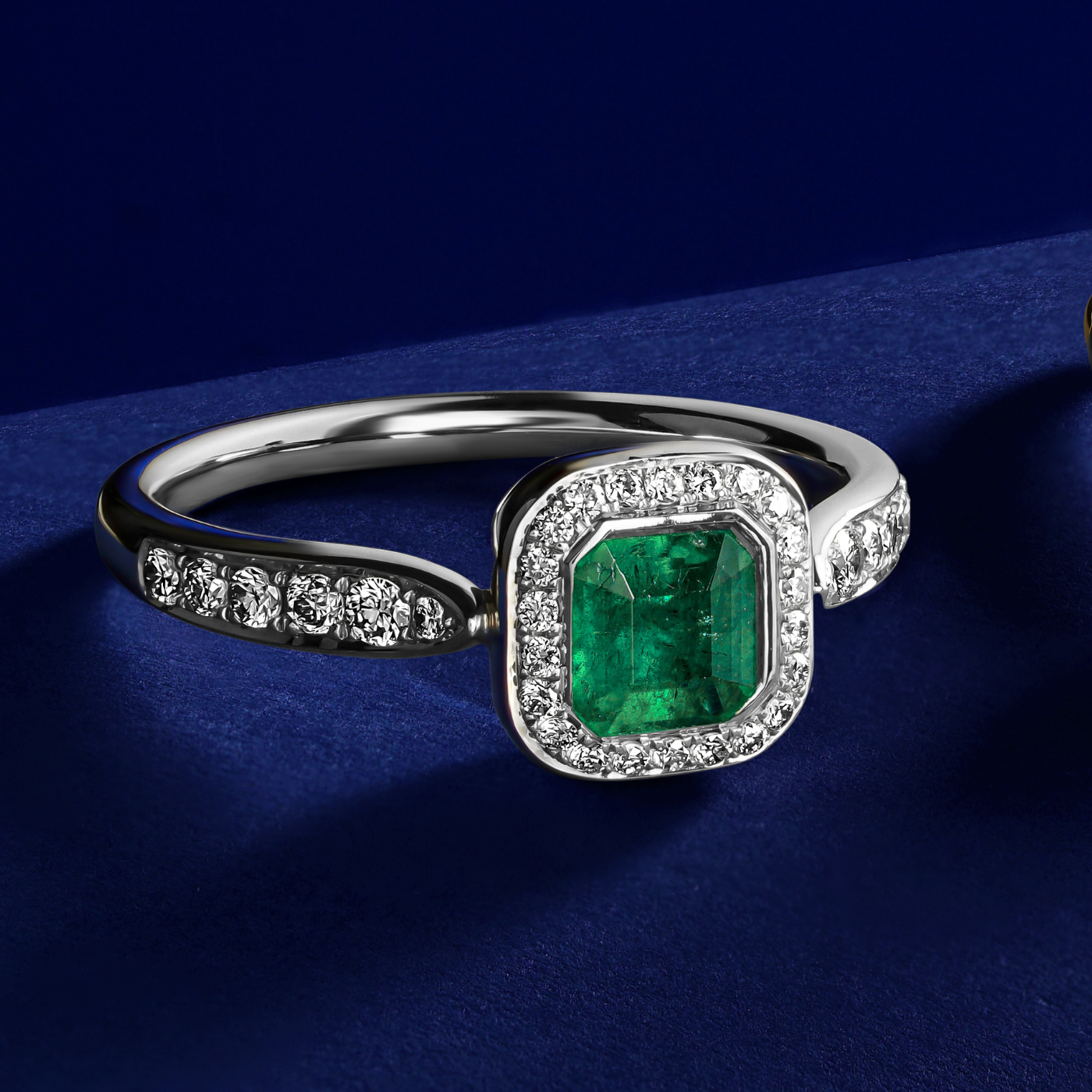 Royal harmony ring with bigger tie emerald surrounded by pave diamonds and on the shank designed by carati jewelry in montreal canada 18k 14 k in zoom and blue backround