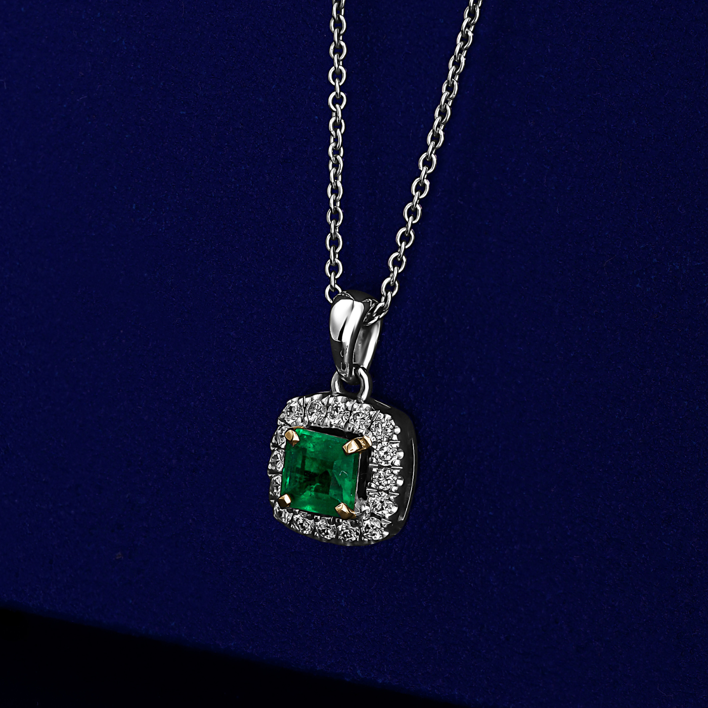 An elegant square pendant necklace with a central emerald surrounded by pave diamonds in sophisticated spark designed by carati jewelry in montreal canada in 18 k 14 k in blue backround
